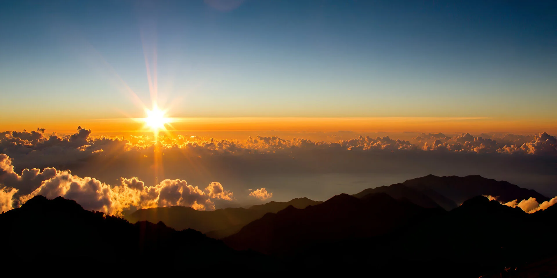 Sunrise breaking over a high mountain range above a layer of cloud, Maui high country, Hawaii