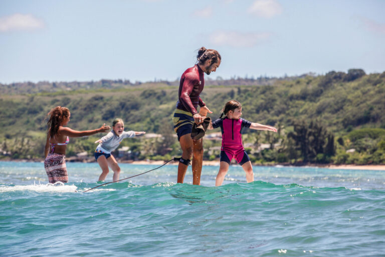 Instructor helping young children ride small waves on the North Shore of Oahu