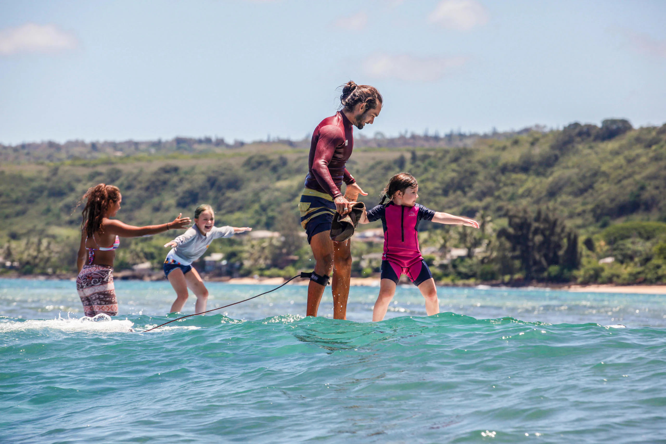 Instructor helping young children ride small waves on the North Shore of Oahu