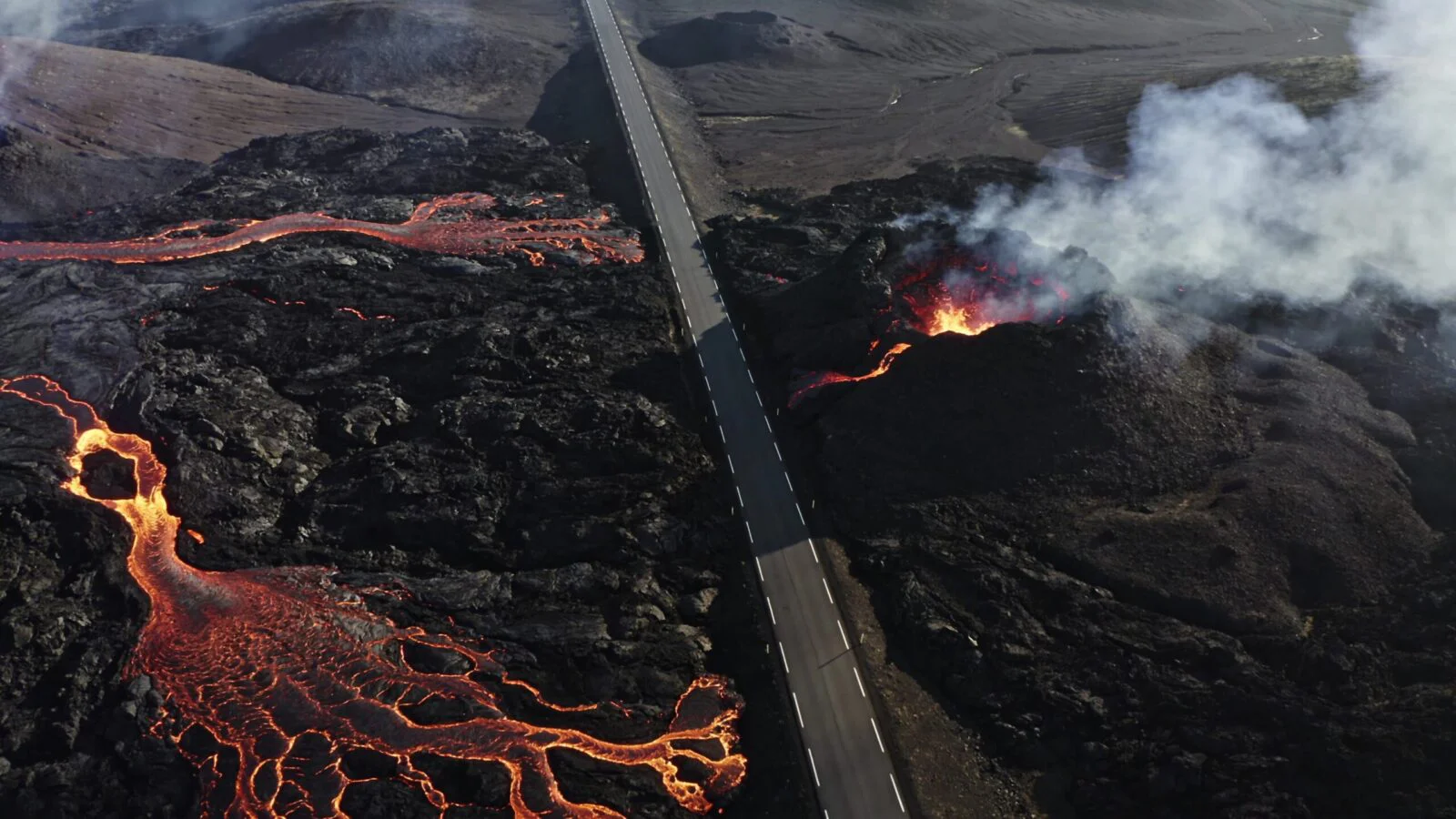 Aerial view of an erupting volcano with glowing lava streams running through dark terrain